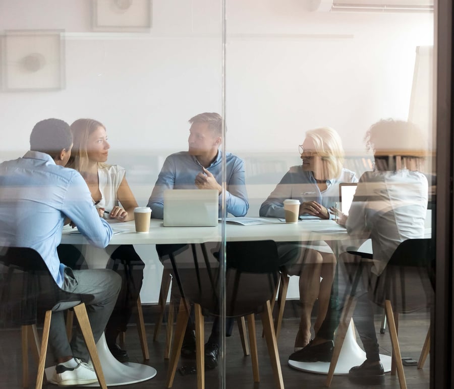 Fem personer som sitter på ett kontor i ett mötesrum och diskuterar